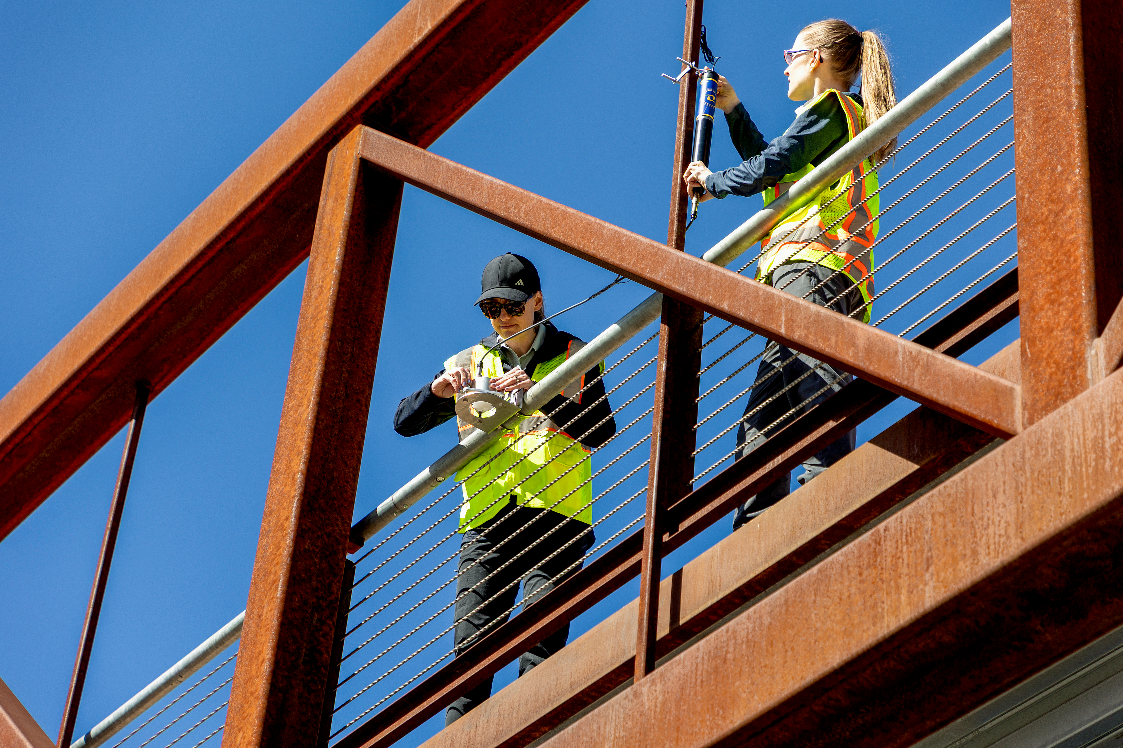 Two people standing on a bridge installing devices to the bridge.
