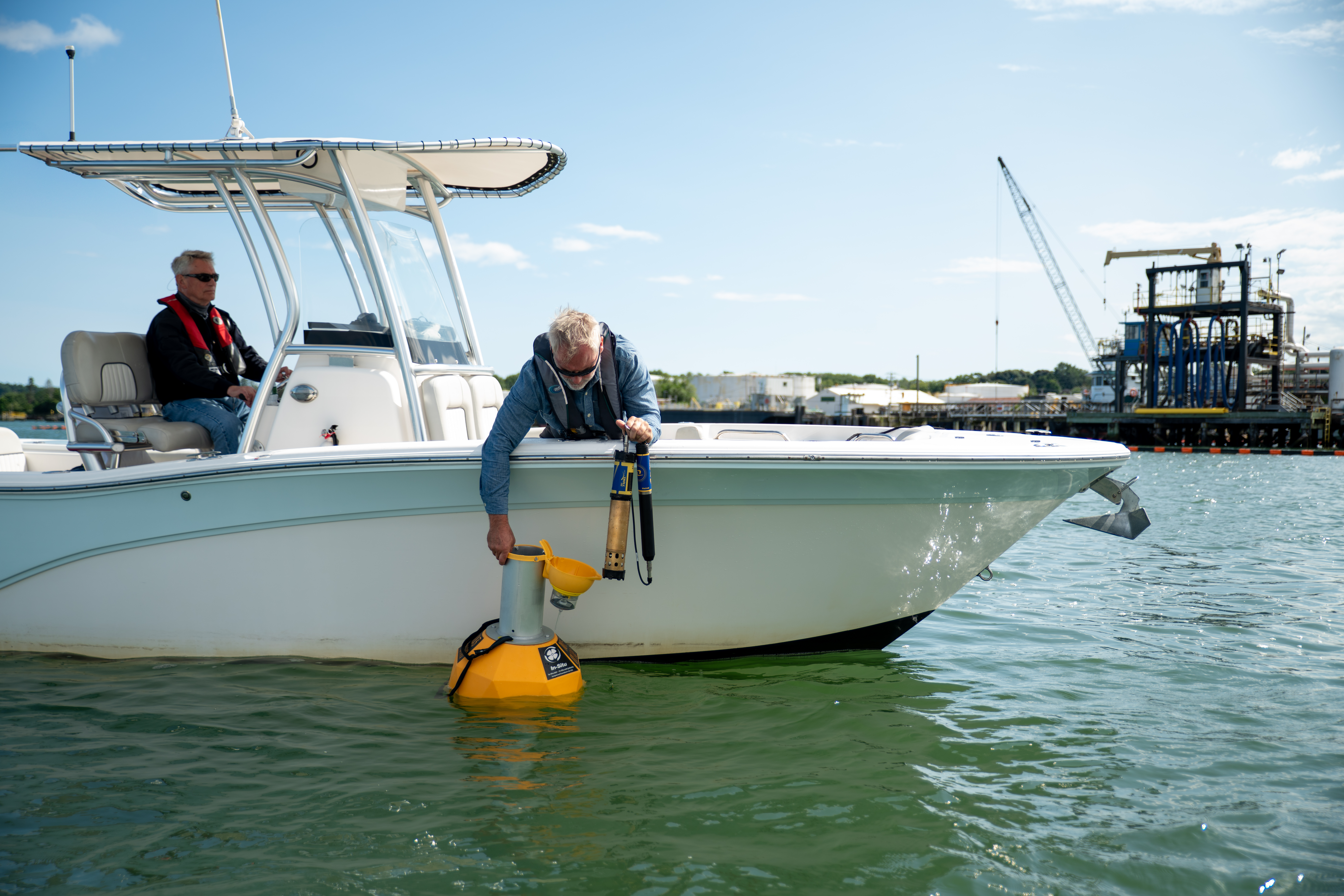  A man leaning over a boat opening the top of a yellow buoy.