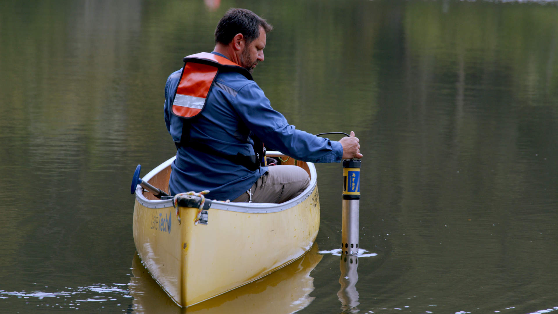 A guy on a boat in a lake putting something in the water.
