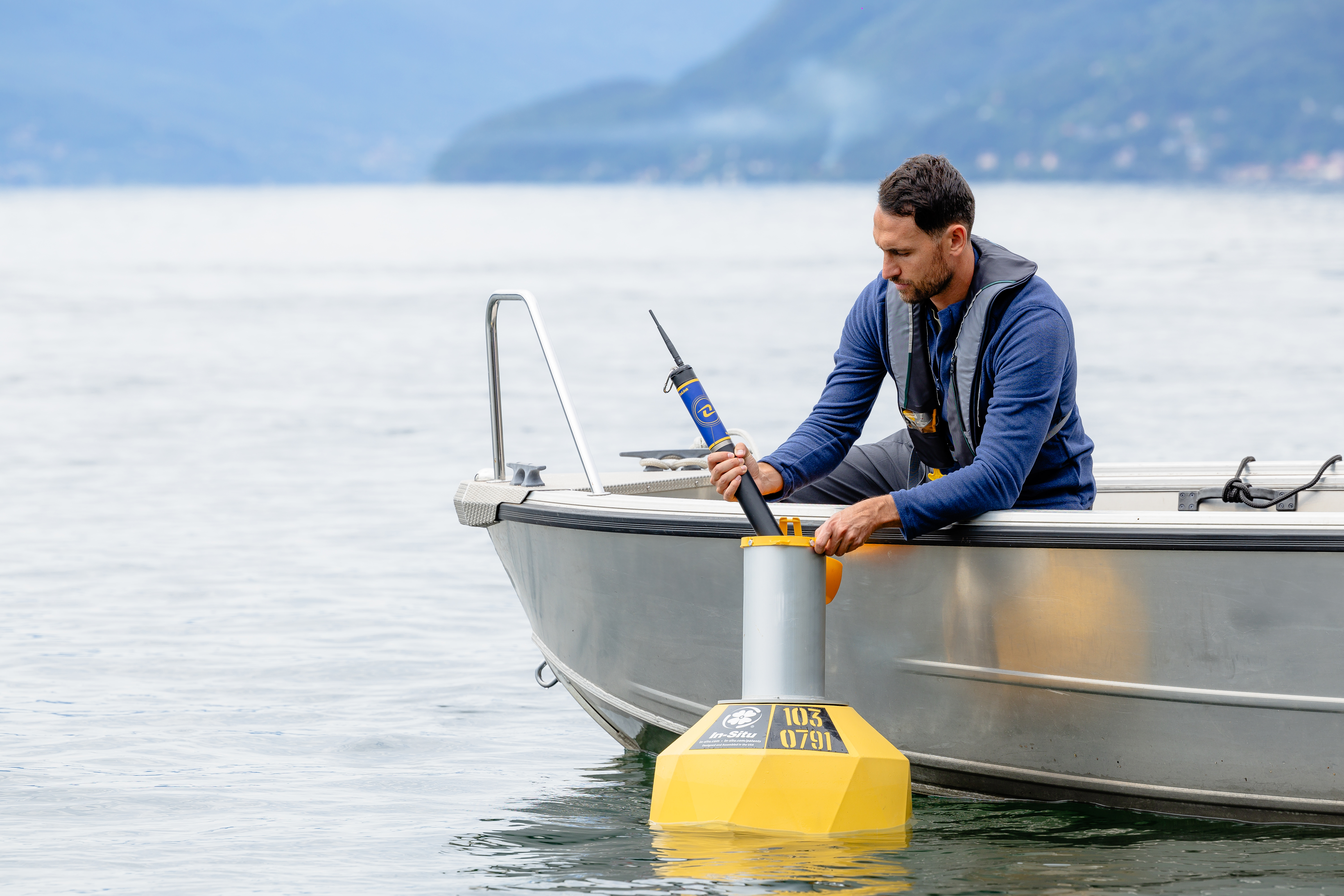 A guy on a boat in a lake putting a device into a yellow buoy.